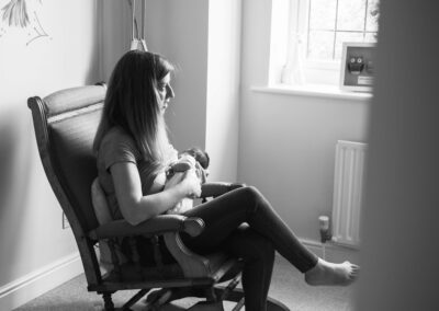 mum breastfeeding newborn baby in chair by window light black and white
